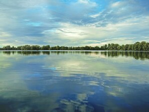 Un lago tranquilo con una ribera boscosa y un cielo parcialmente nublado.