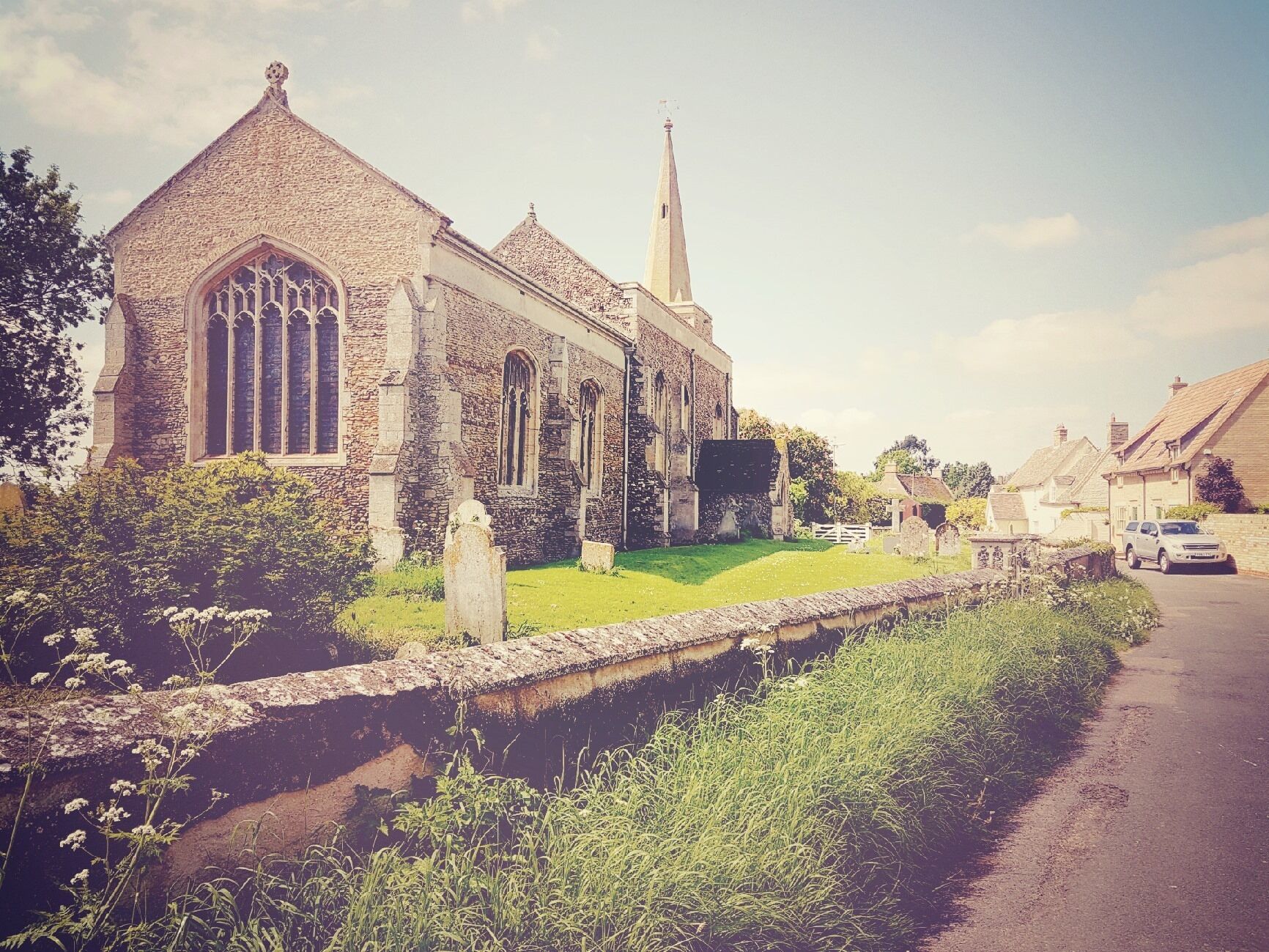 A historic church with a prominent spire, stone walls, and a well-maintained lawn.