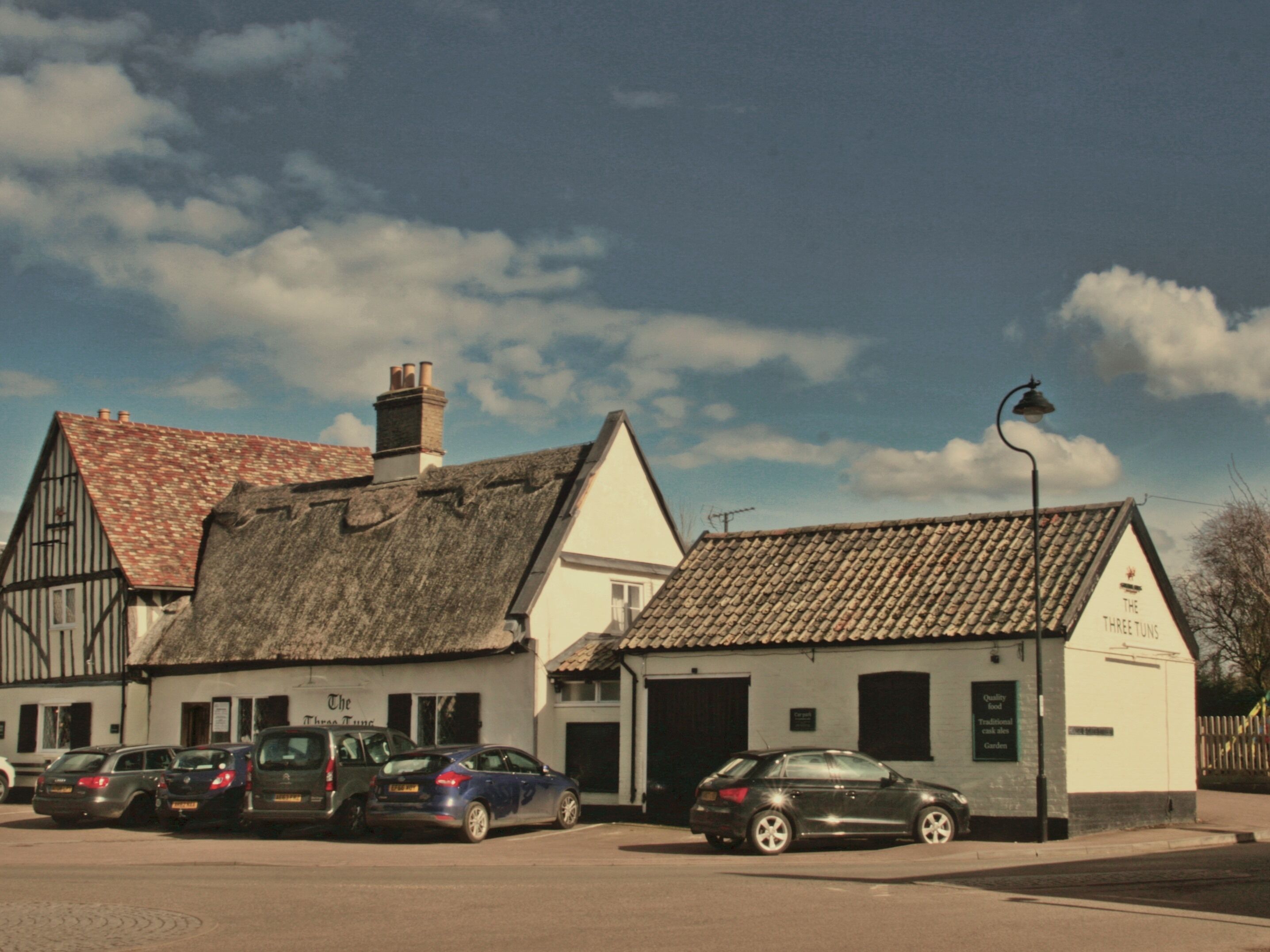 A traditional building with a thatched roof and a tiled roof, parked cars in front, and a clear sky.
