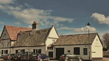 A traditional building with a thatched roof and a tiled roof, parked cars in front, and a clear sky.