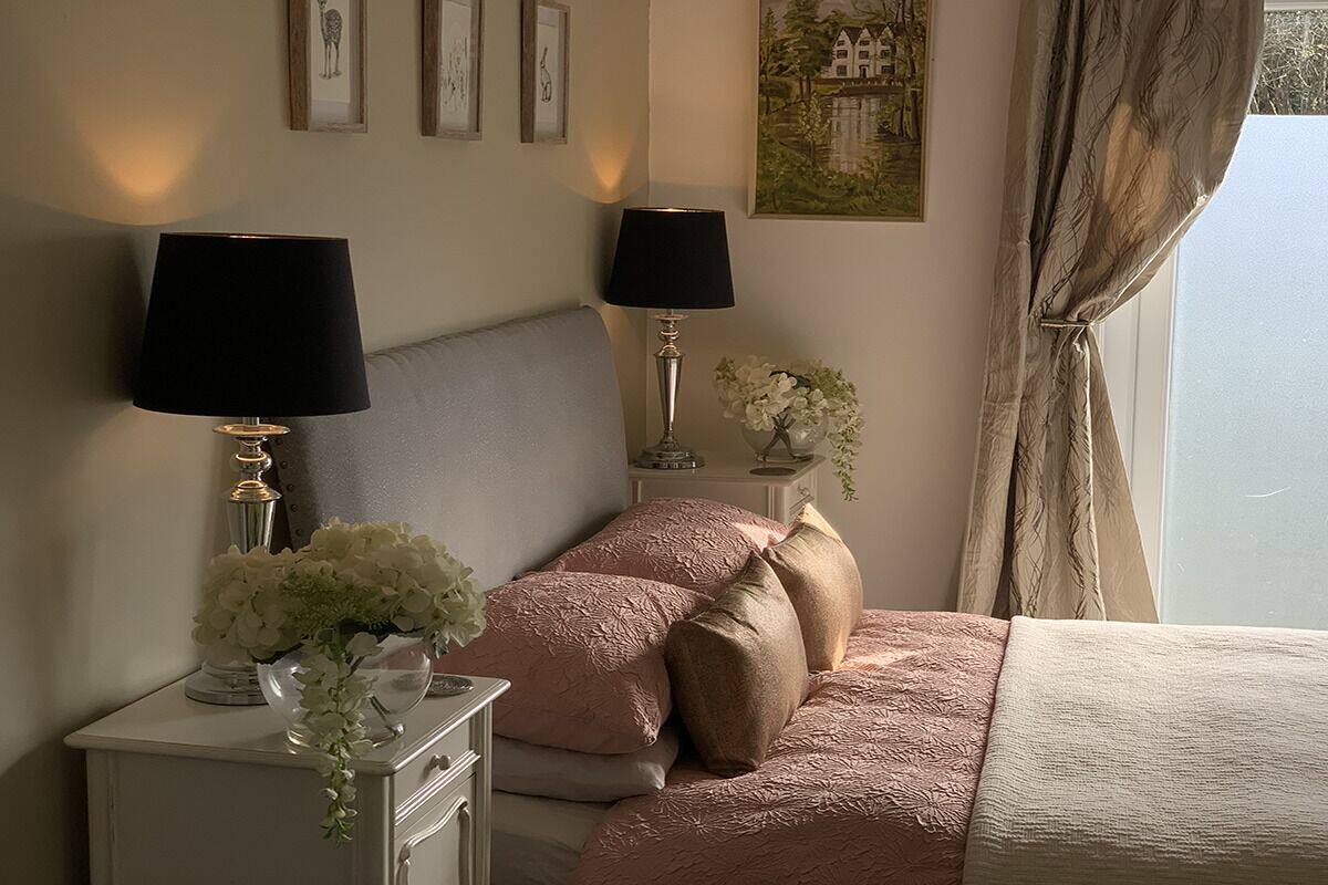 A bedroom with a bed, two bedside tables with lamps, a vase of flowers, and a painting on the wall.