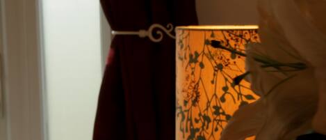 A room with a lamp on a table, a curtain, and a wall with a floral pattern.