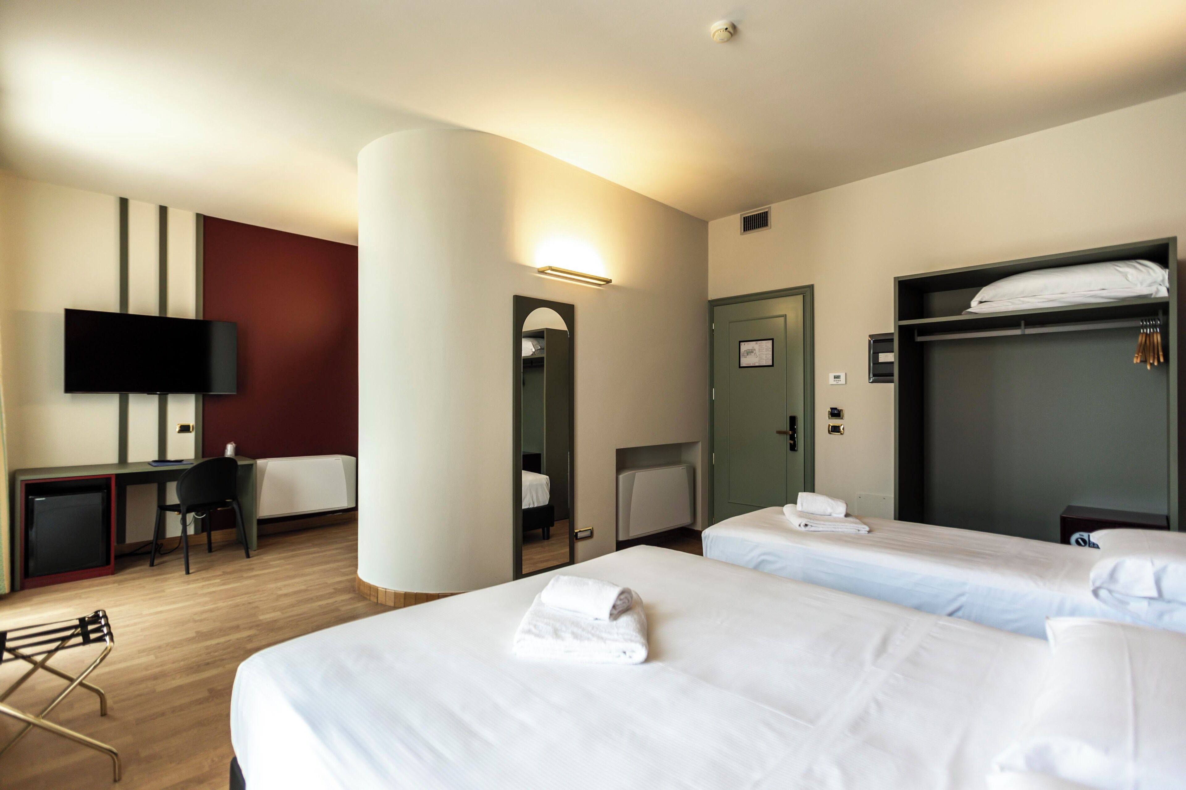 A hotel room with two beds, a desk, a chair, a TV, and a wardrobe.