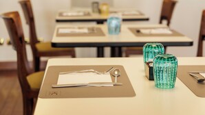A dining table with a placemat, cutlery, and two green glass vases. - HC Hotel Cremona Pilgrim's (Cicognolo)