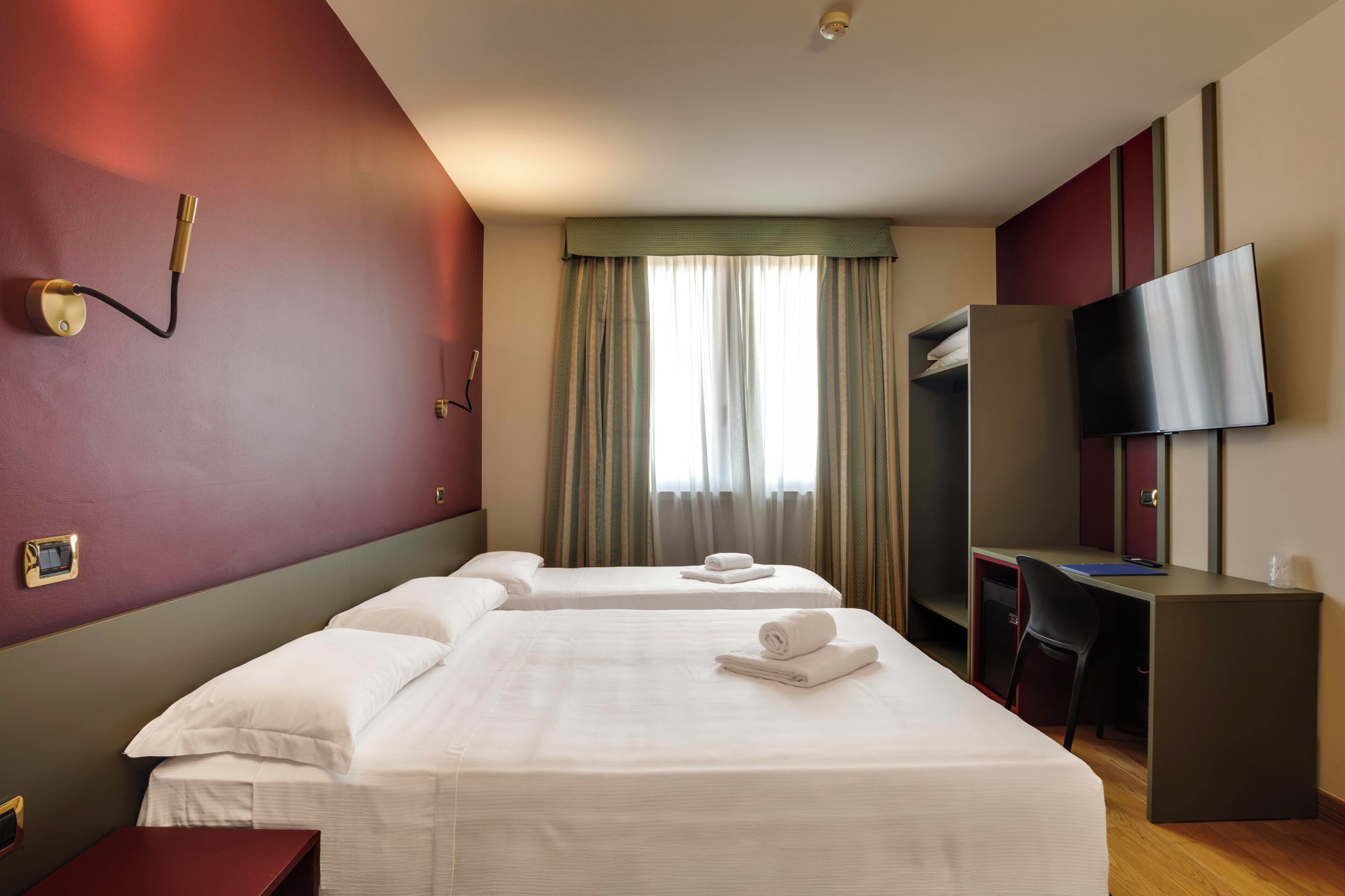 Una habitación de hotel con dos camas, un escritorio, un televisor y un armario.