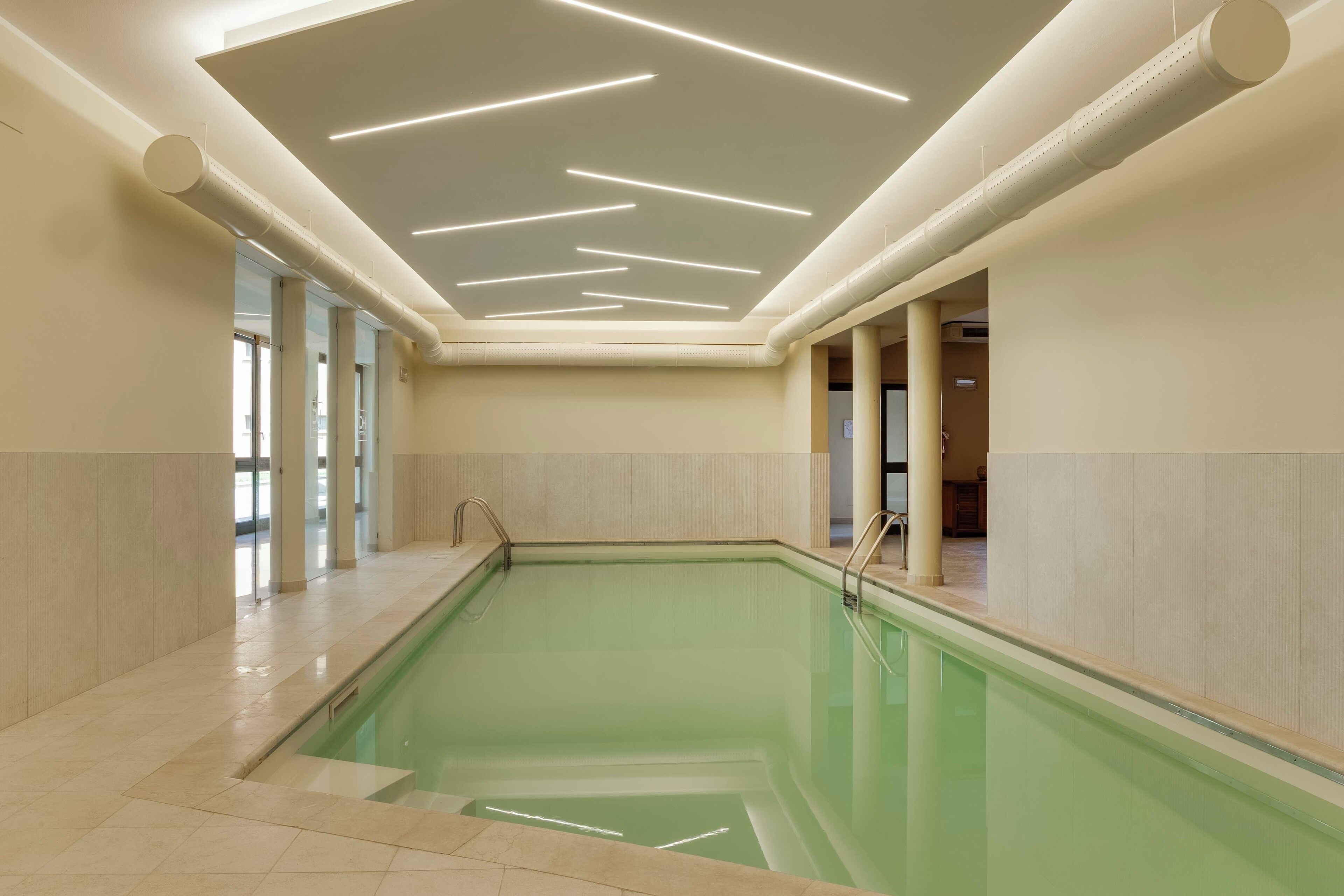 A swimming pool with a modern ceiling design, tiled walls, and a clear view of the adjacent room.