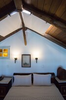 Un dormitorio acogedor en el ático, con techo inclinado, una cama con ropa blanca, dos lámparas de pared y un cuadro en la pared.