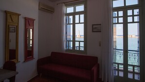 Una habitación con un sofá rojo, dos ventanas con cortinas y vista al mar.