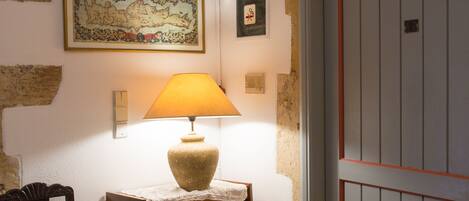 Une pièce avec un plancher en bois, une lampe sur une petite table, une chaise, un extincteur et une porte avec un cadre rouge.