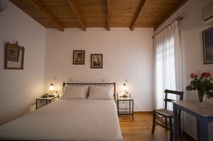 Une chambre avec un plafond en bois, un lit avec une literie blanche, deux tables de chevet avec des lampes, une chaise et un vase rempli de fleurs.