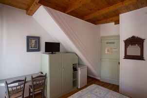 Ein Zimmer mit Holzbalkendecke, einem Schreibtisch mit Stühlen, einem Schrank, einem kleinen Kühlschrank und einer Tür mit Spiegel.