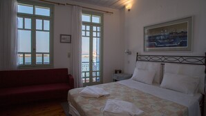Un dormitorio con cama, un sofá rojo, una ventana con cortinas, una mesita de noche y un cuadro en la pared.