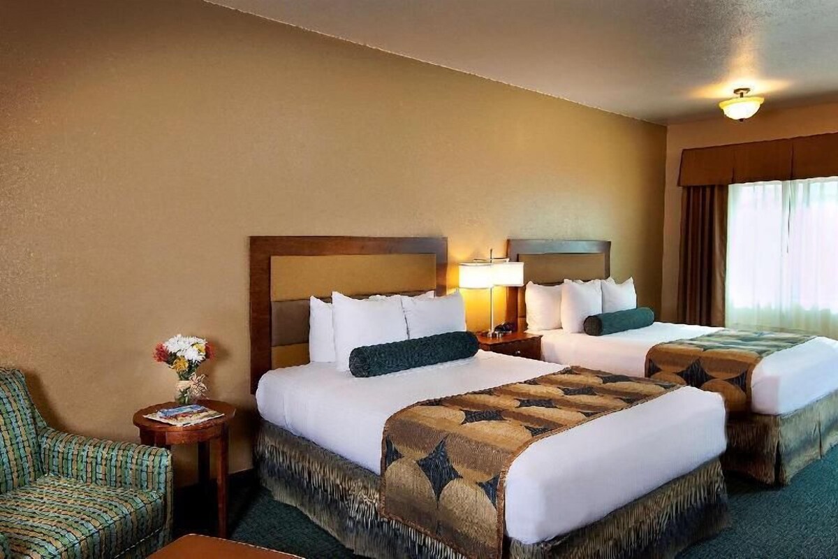 A hotel room with two beds, a chair, a nightstand, and a lamp.