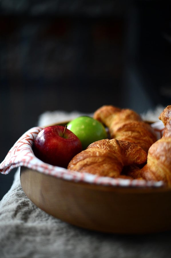 Un cuenco de madera con croissants y manzanas sobre un paño.