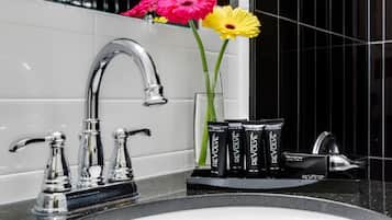 Un baño con un lavabo moderno, grifos cromados y una jarra de cristal con flores.