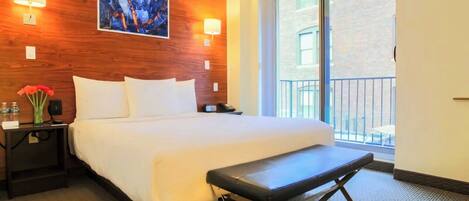 A hotel room with a large bed, a bench, a wooden accent wall, and a large window.