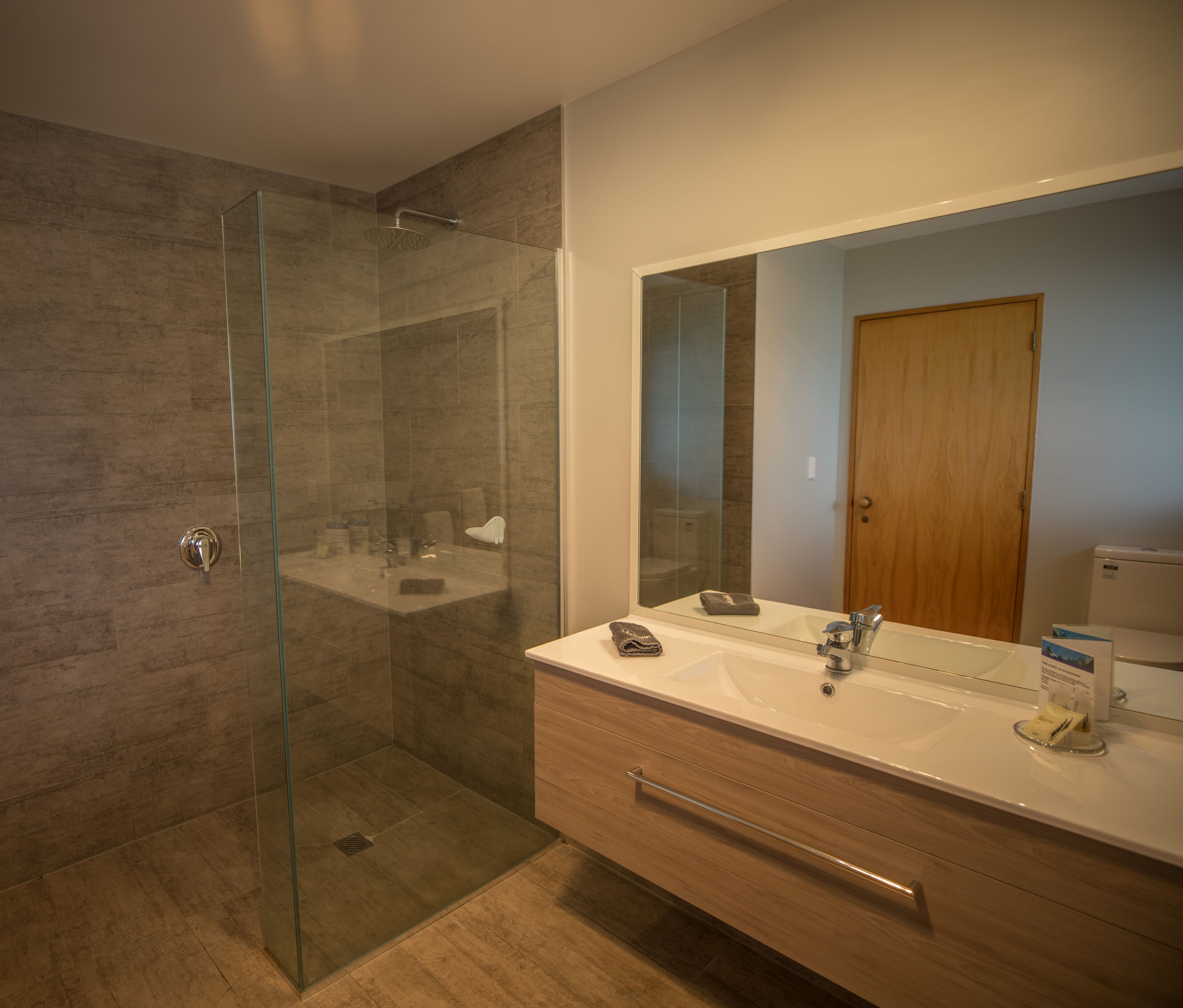 Une salle de bain moderne avec une douche à parois de verre, un grand miroir et un meuble-lavabo en bois.