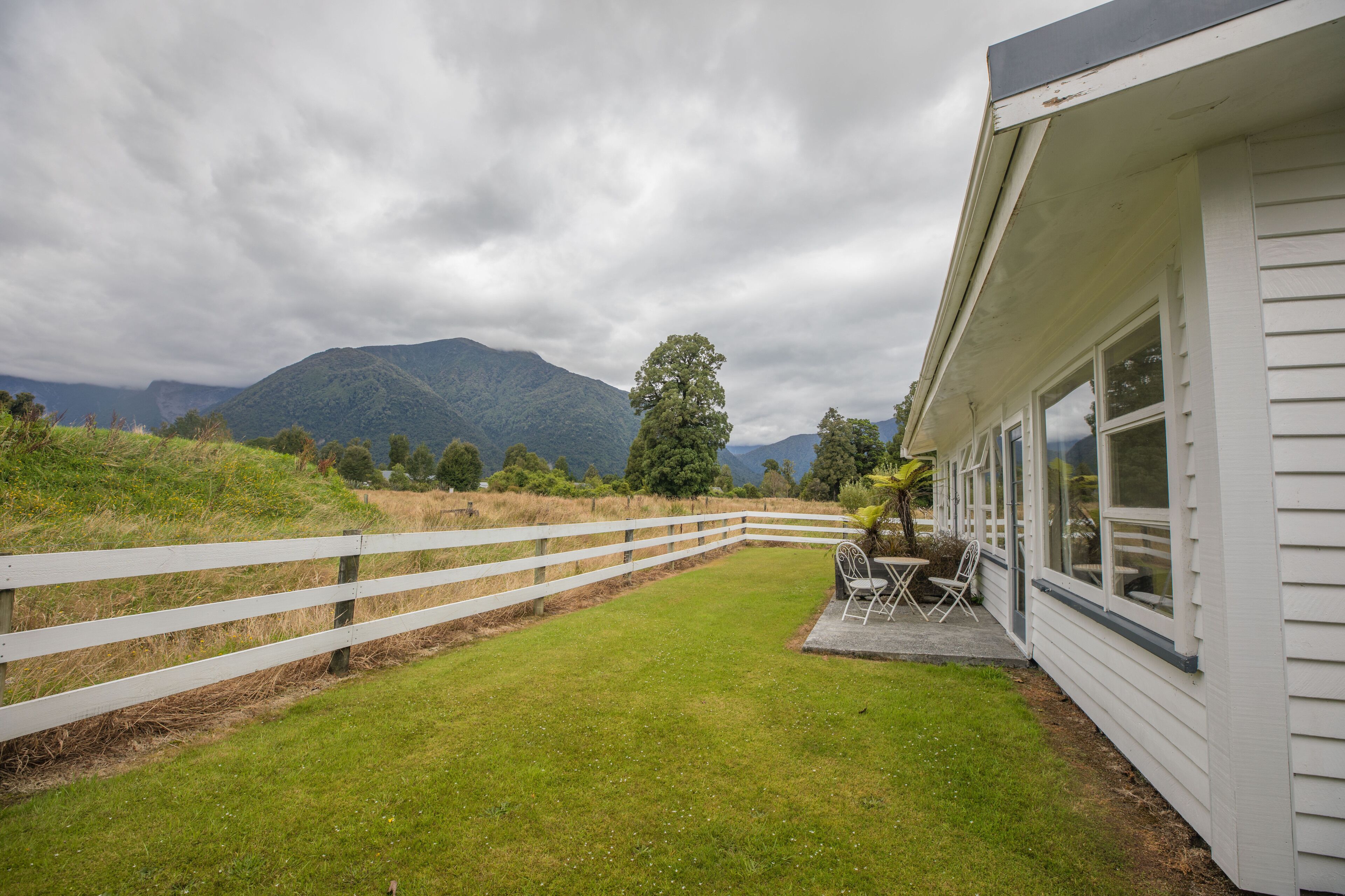 Una casa con fachada blanca, patio cercado y muebles de exterior.
