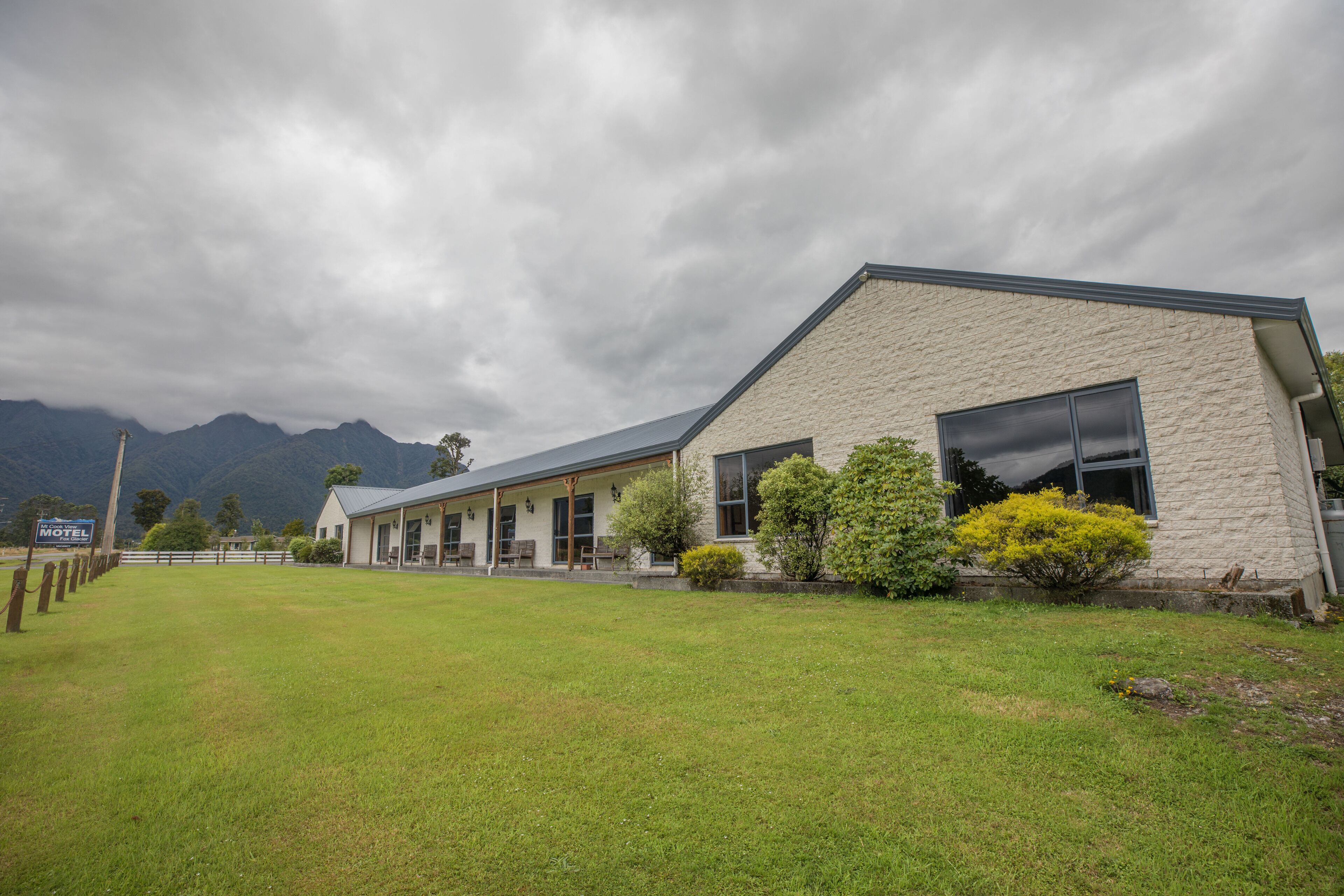 A motel with a stone facade, large windows, and a grassy front yard.