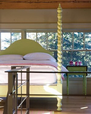 A bed with a wooden headboard, a bedside table, and a window with a view of trees.