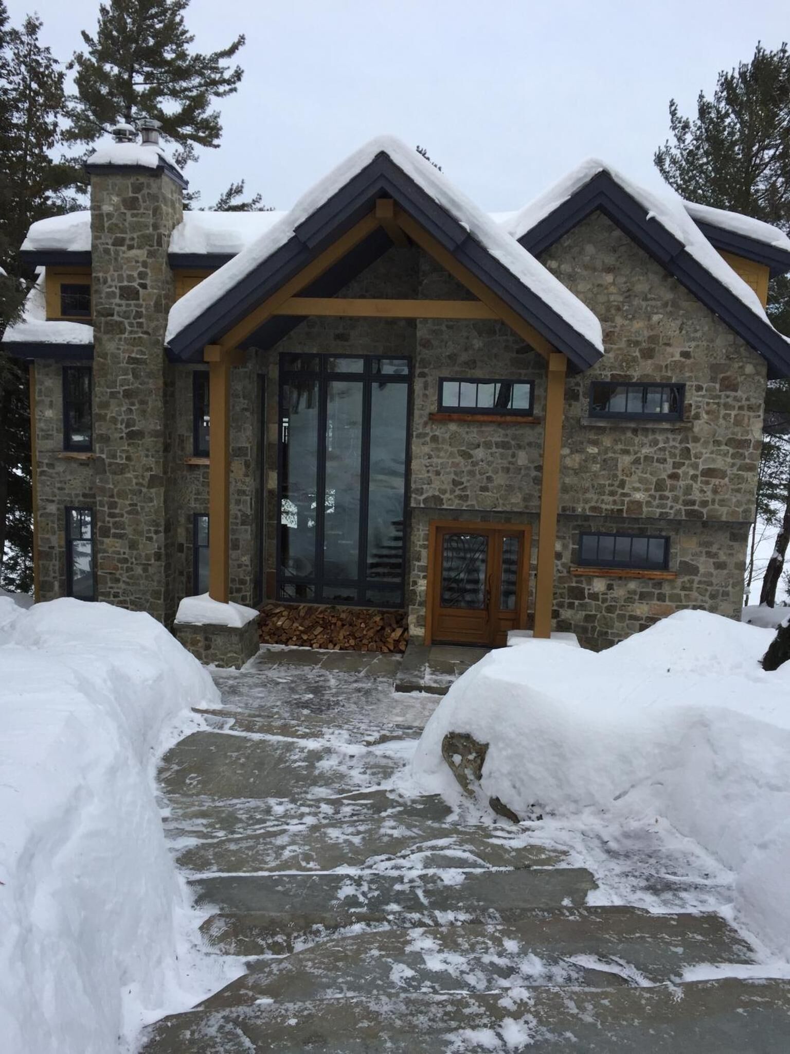 A stone building with a large glass door and windows, surrounded by snow.