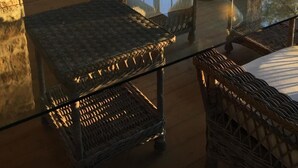 Una habitación acogedora con mobiliario de mimbre, una mesa de vidrio y amplias ventanas que ofrecen vistas a árboles y un lago.