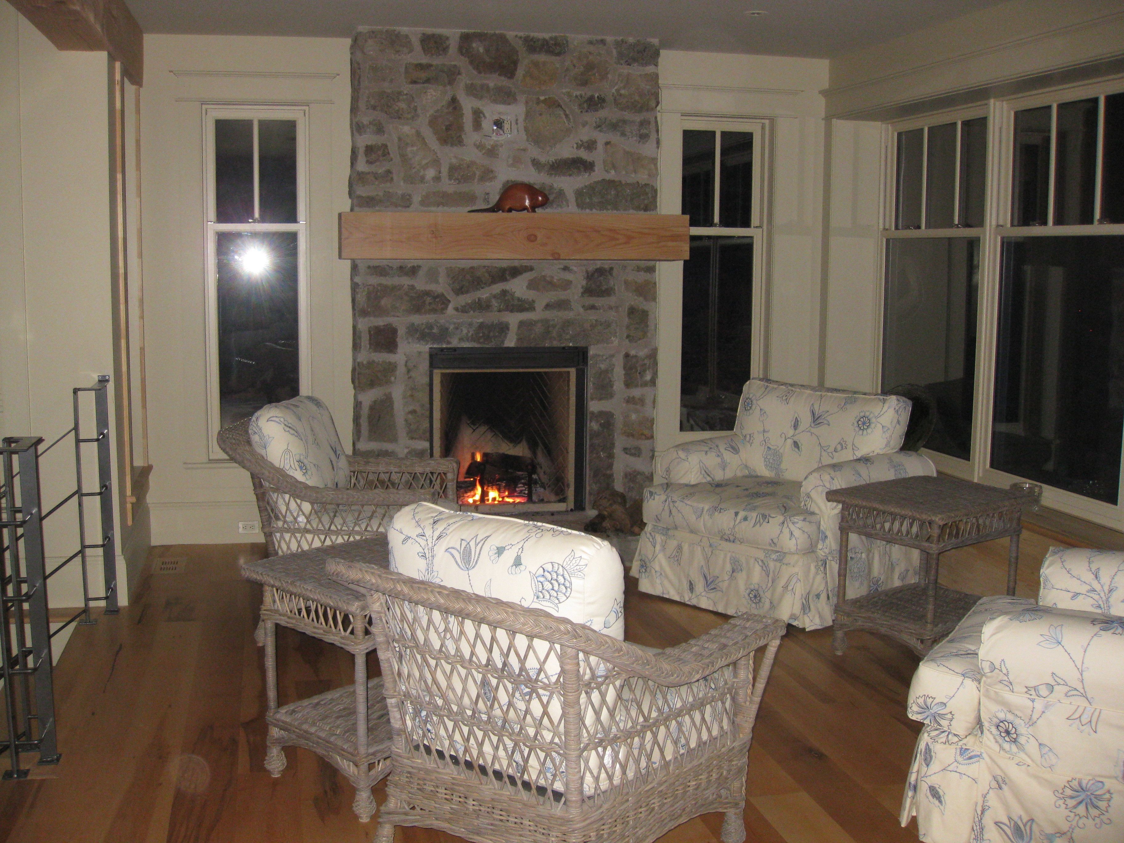 A cozy living room with wicker furniture, a stone fireplace, and large windows.