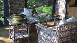 Una habitación soleada con muebles de mimbre, una mesa de vidrio y vistas al verdor a través de amplios ventanales.