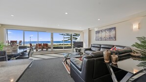 A modern living room with a large glass door leading to a balcony with a view of the beach. - The Pavilions Beachfront Apartments (Tauranga)