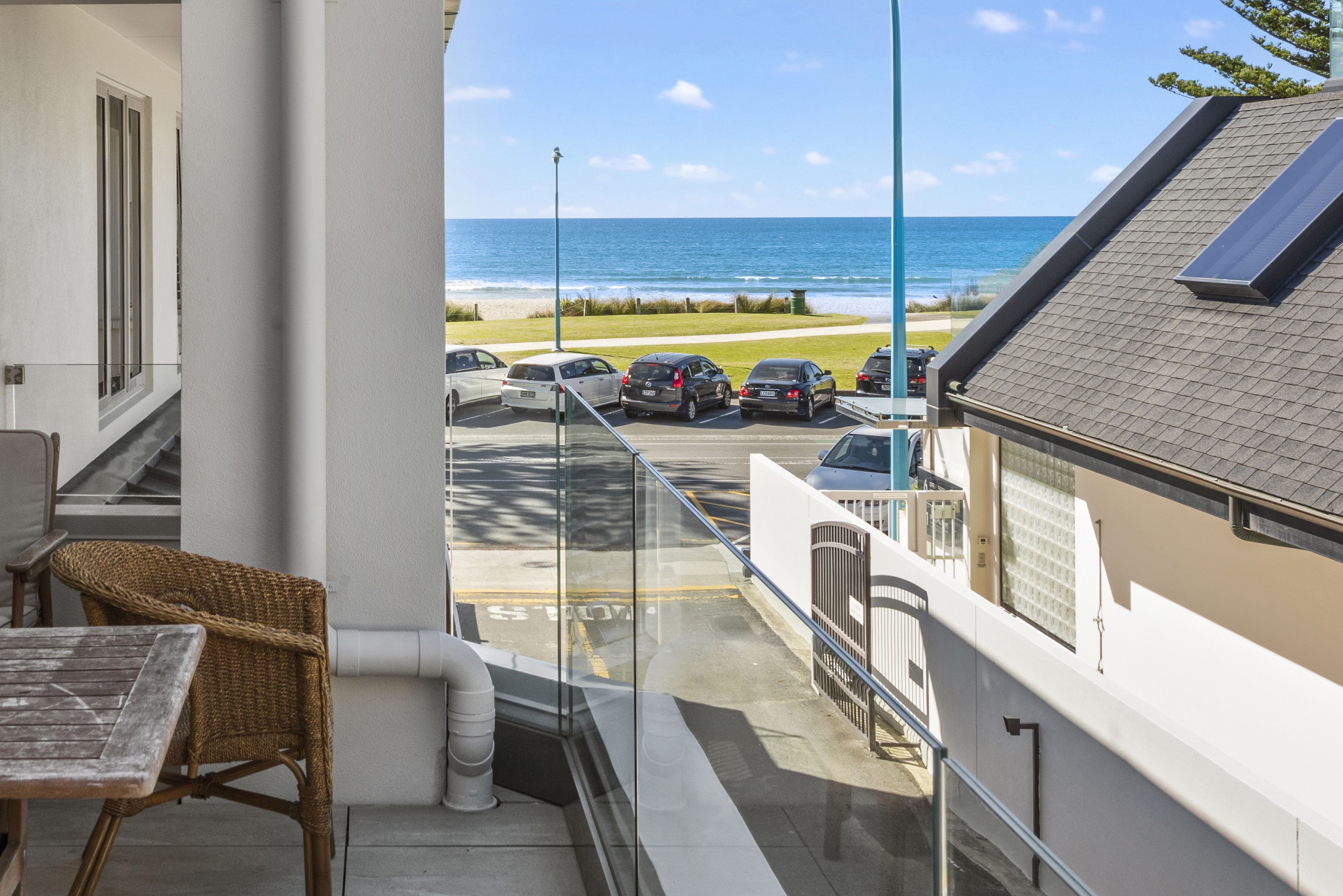 A balcony with a view of the beach and parked cars.