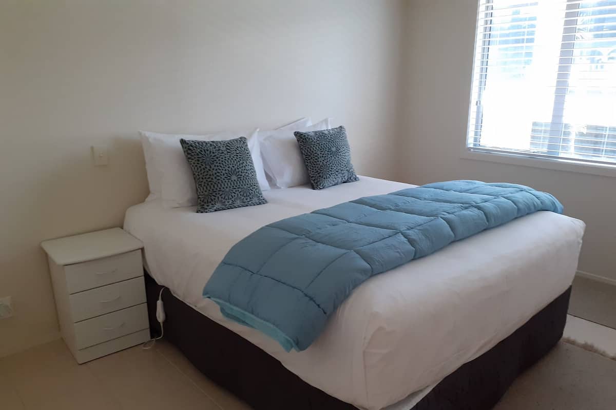 A bedroom with a bed, a bedside table, and a window.