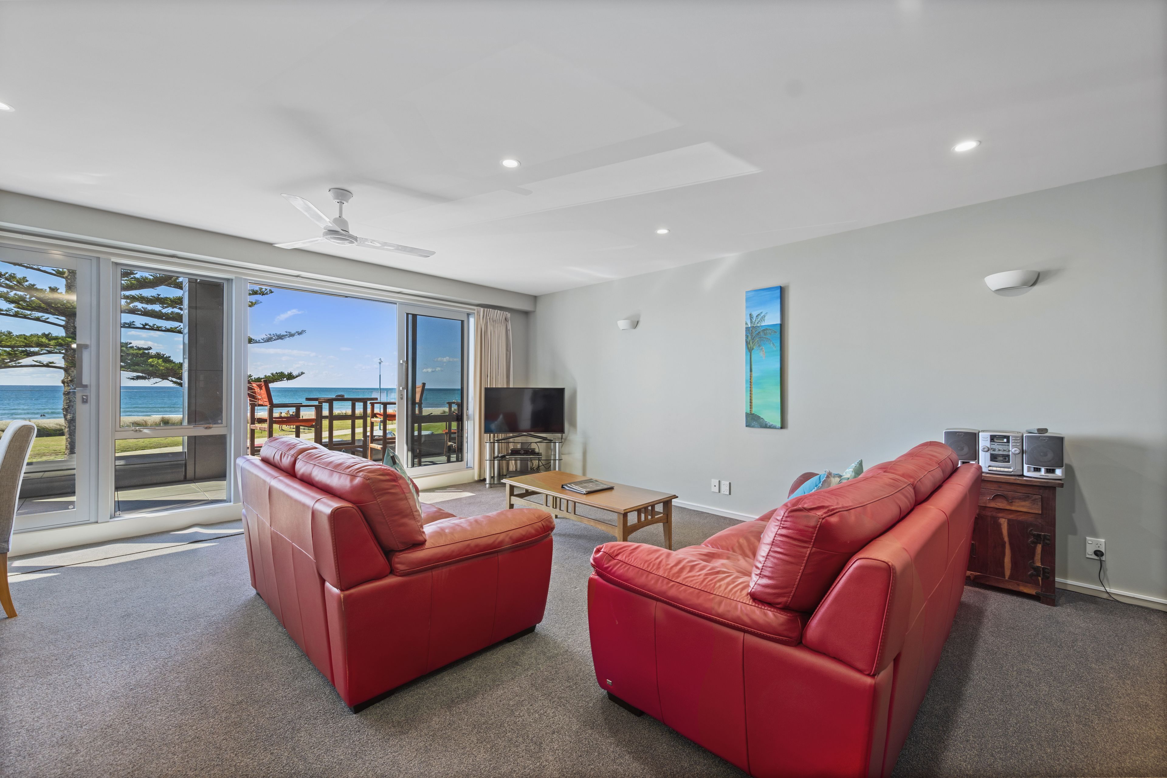 A spacious living room with a red leather sofa, a wooden coffee table, and a flat-screen TV.