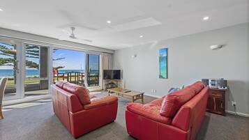 A spacious living room with a red leather sofa, a wooden coffee table, and a flat-screen TV.
