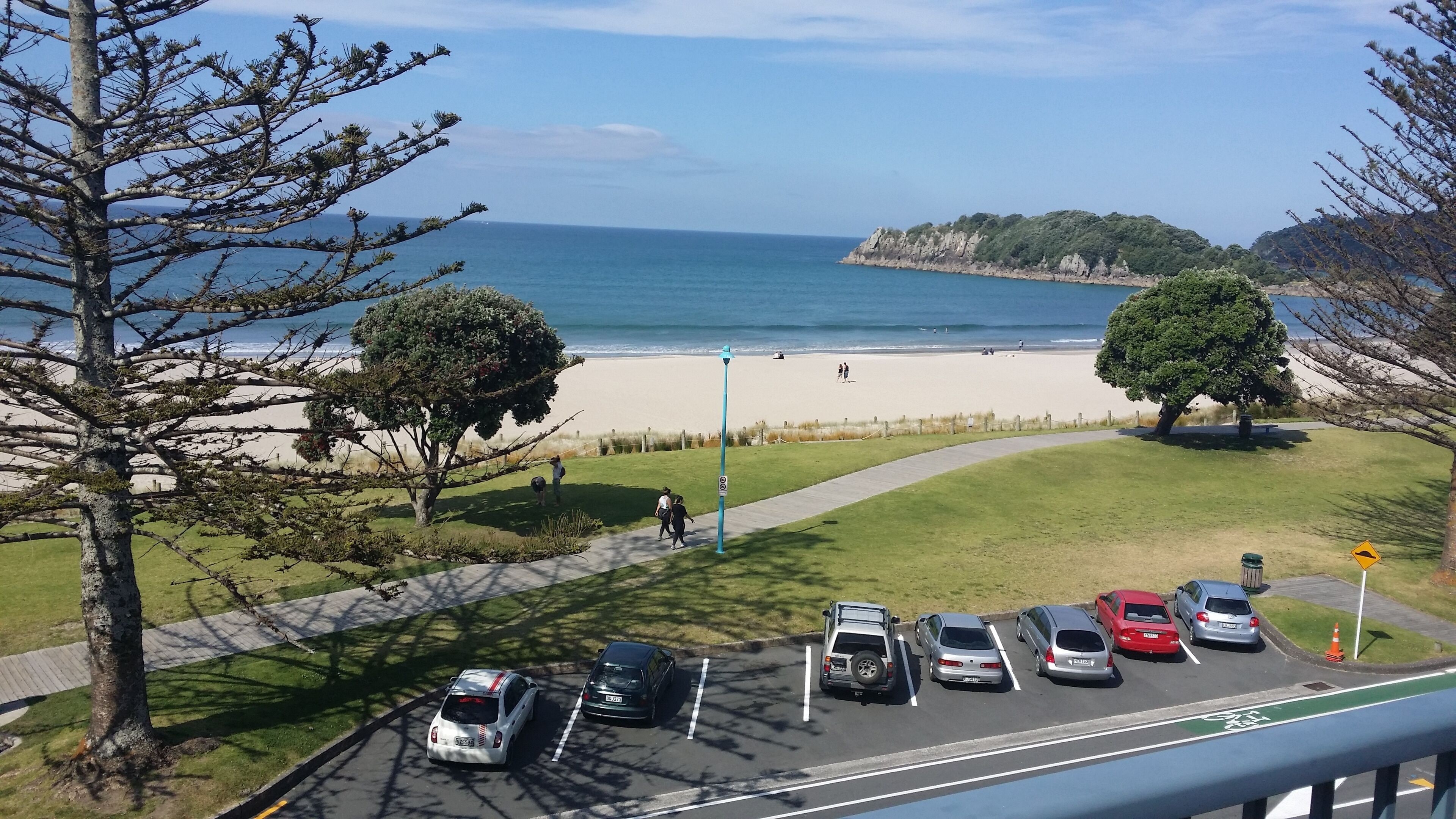 Ein Parkplatz mit Autos, ein Weg zum Strand und Blick aufs Meer.
