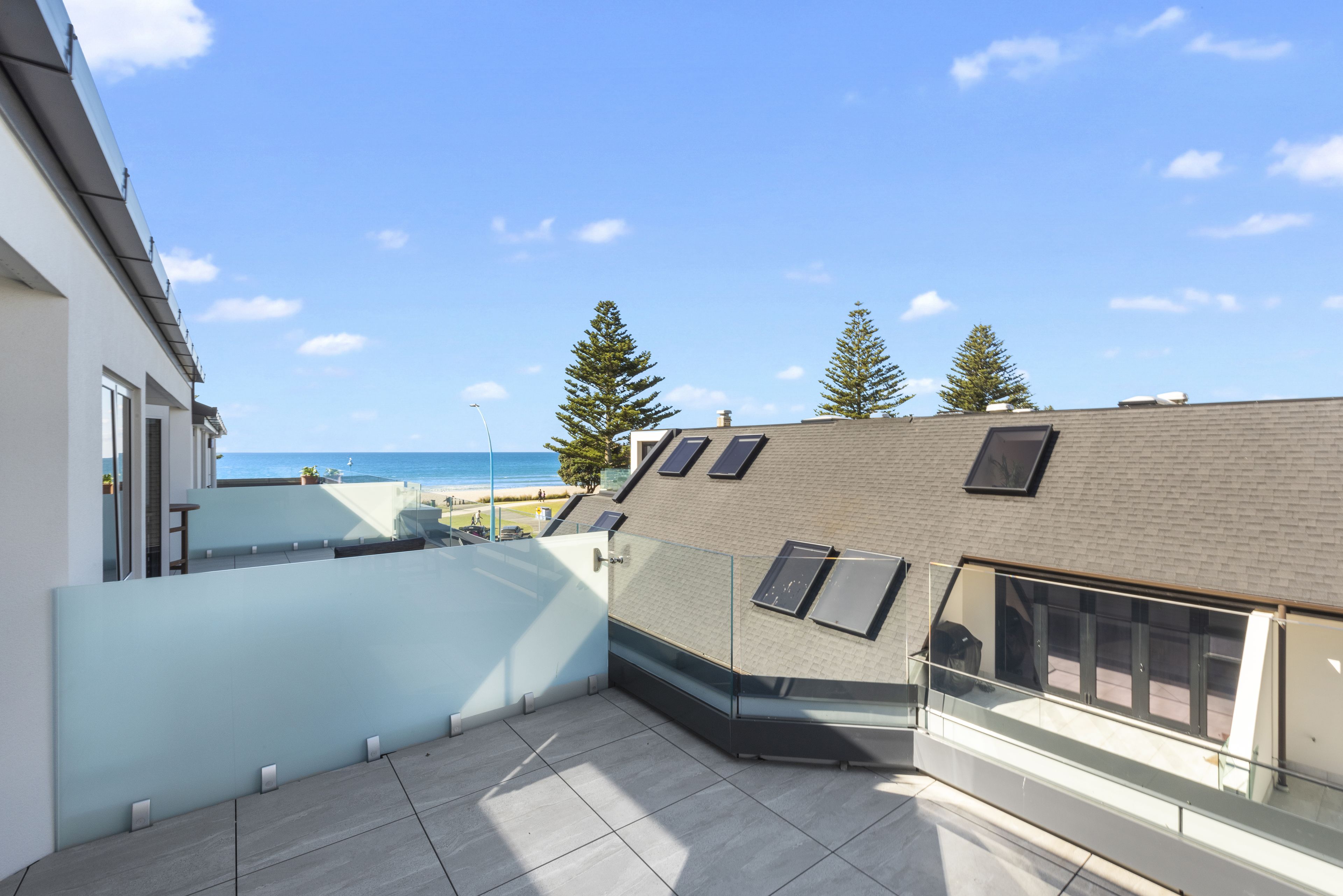 Une terrasse sur le toit offrant une vue sur la mer, une balustrade en verre et un bâtiment en briques.