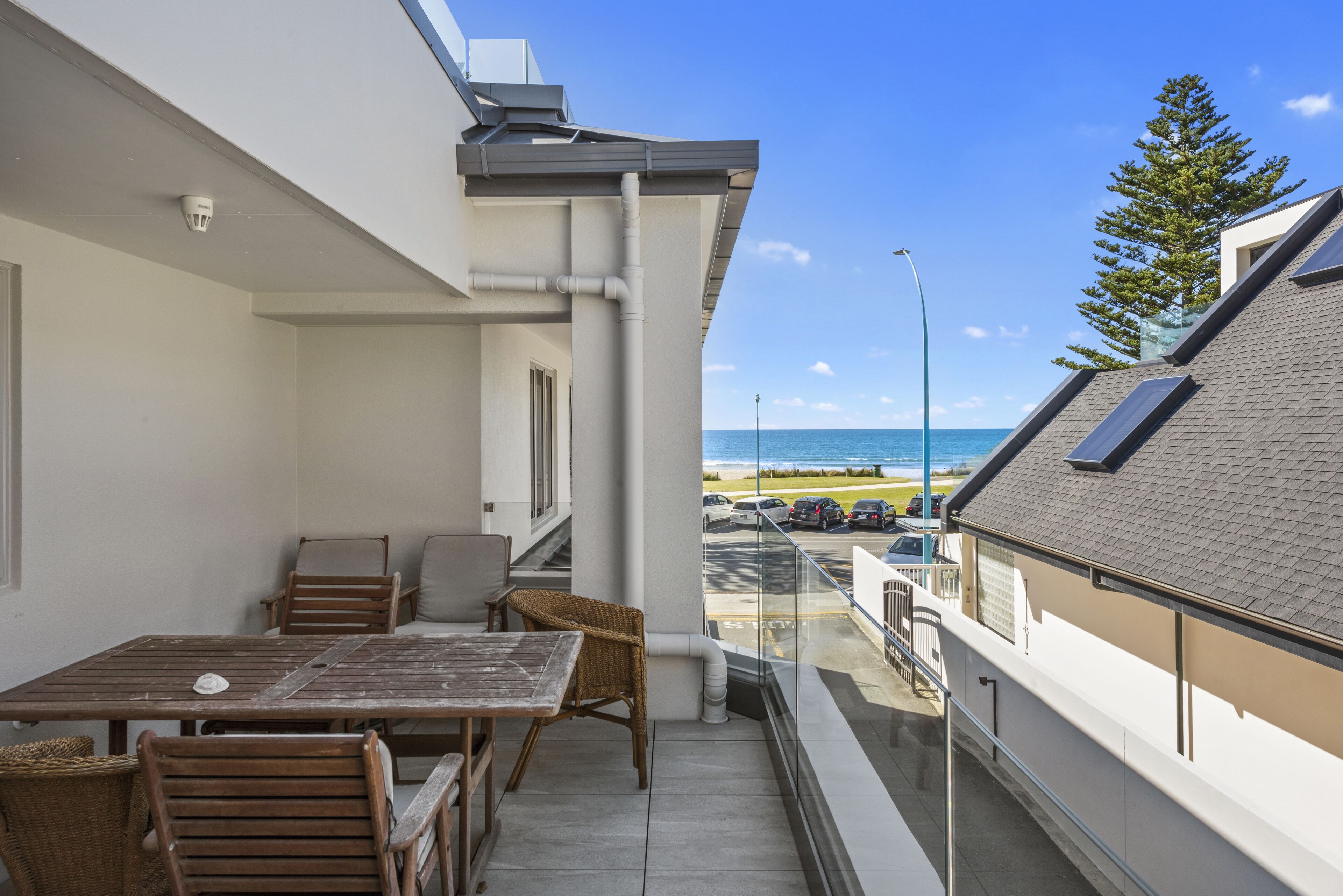 A balcony with a table and chairs, overlooking a beach and parked cars.