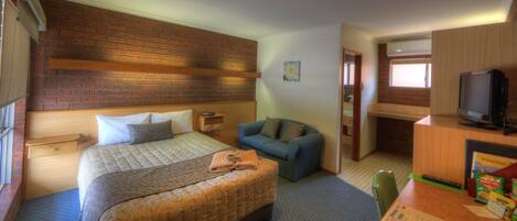 A hotel room with a large bed, a blue sofa, a wooden desk with a television, and a brick wall.