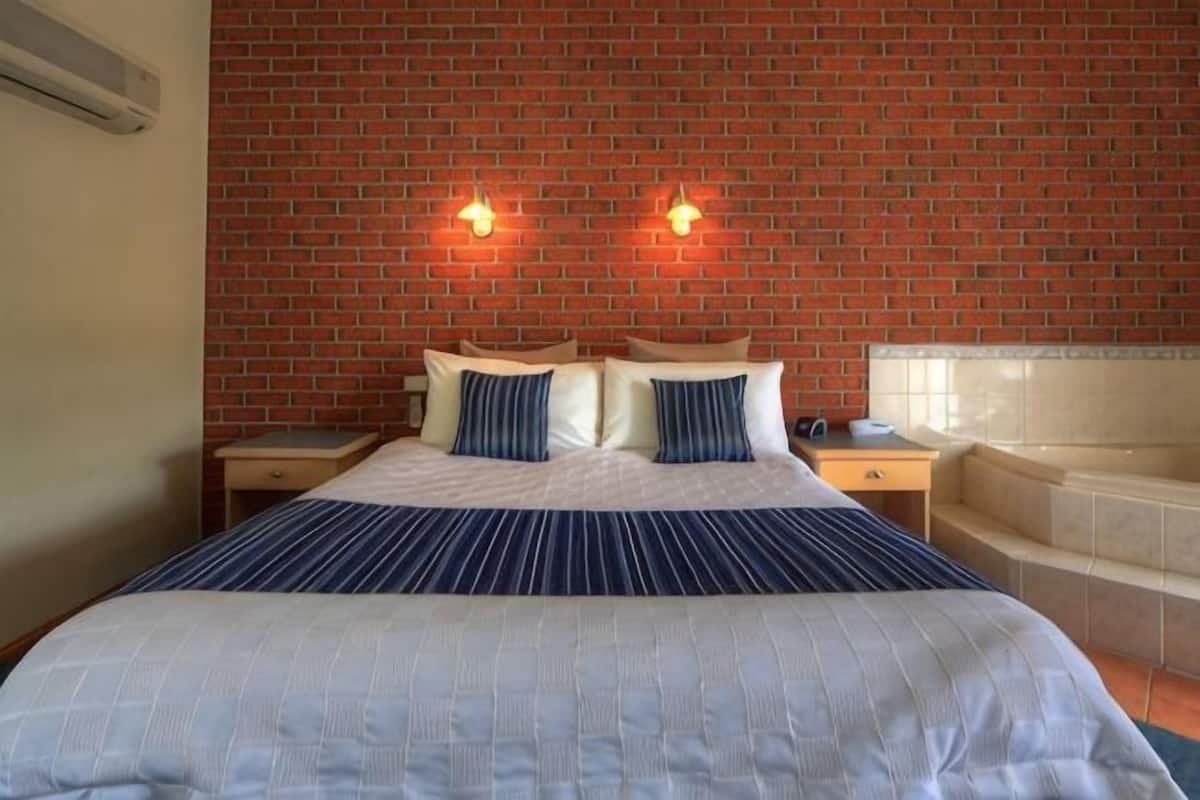 Une chambre dâhĂŽtel avec un mur en briques, un lit recouvert dâune courtepointe Ă rayures, deux lampes de chevet, une table de chevet et une baignoire.