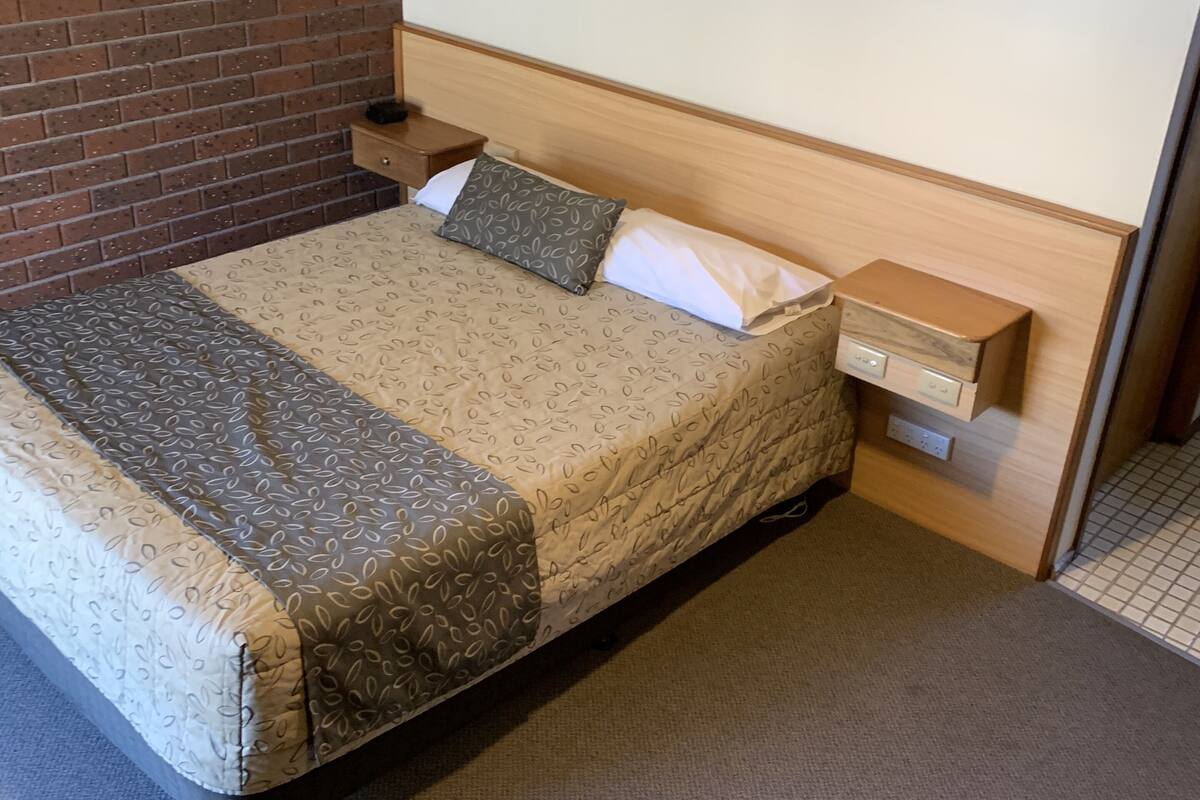 A hotel room with a bed, a nightstand, a wooden headboard, and a brick wall.
