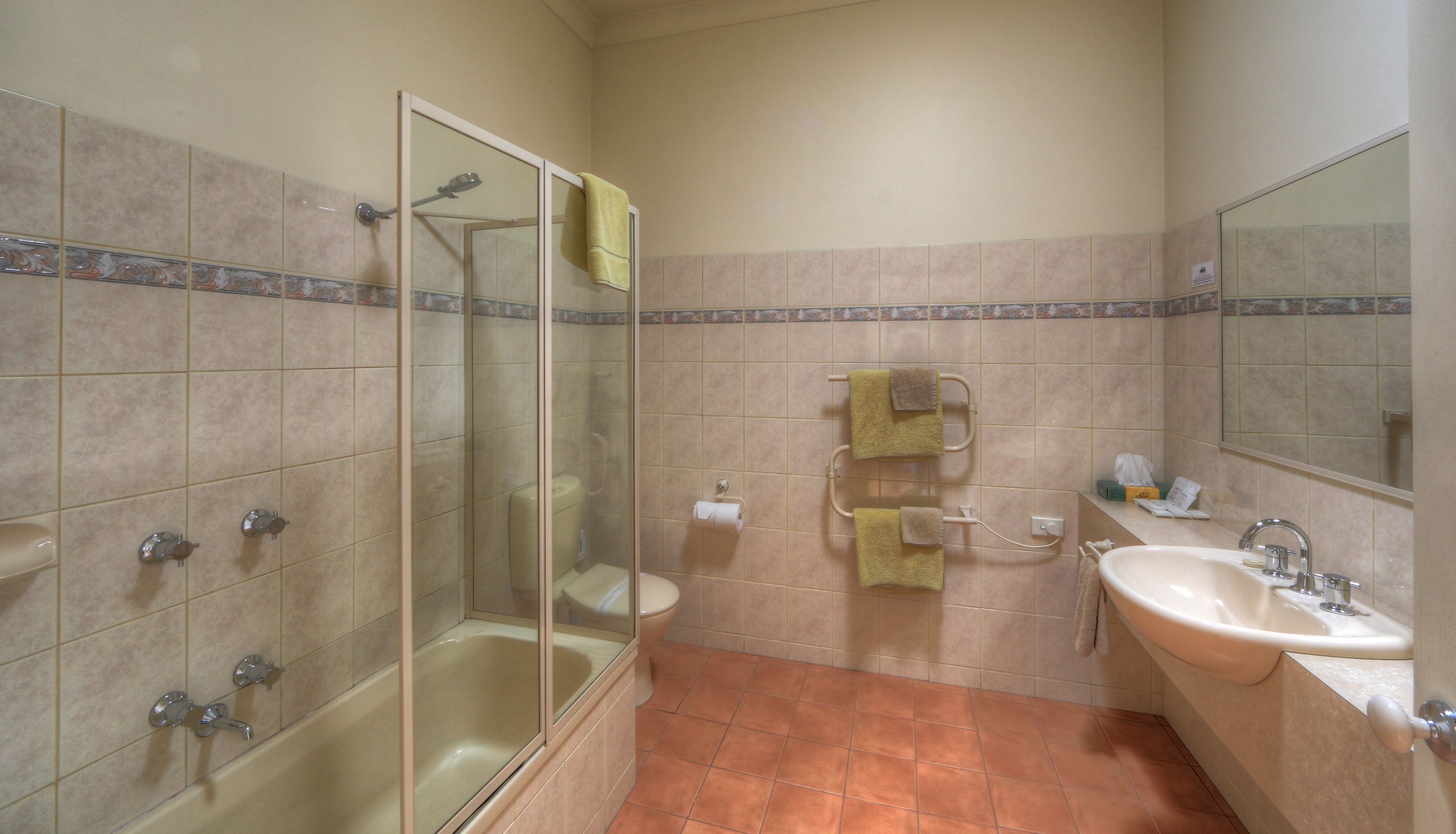 Un baño con ducha separada por mampara de cristal, inodoro, lavamanos y espejo.