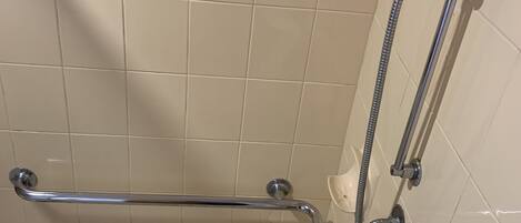 A shower area with a grab bar, a handheld showerhead, and a wall-mounted faucet.