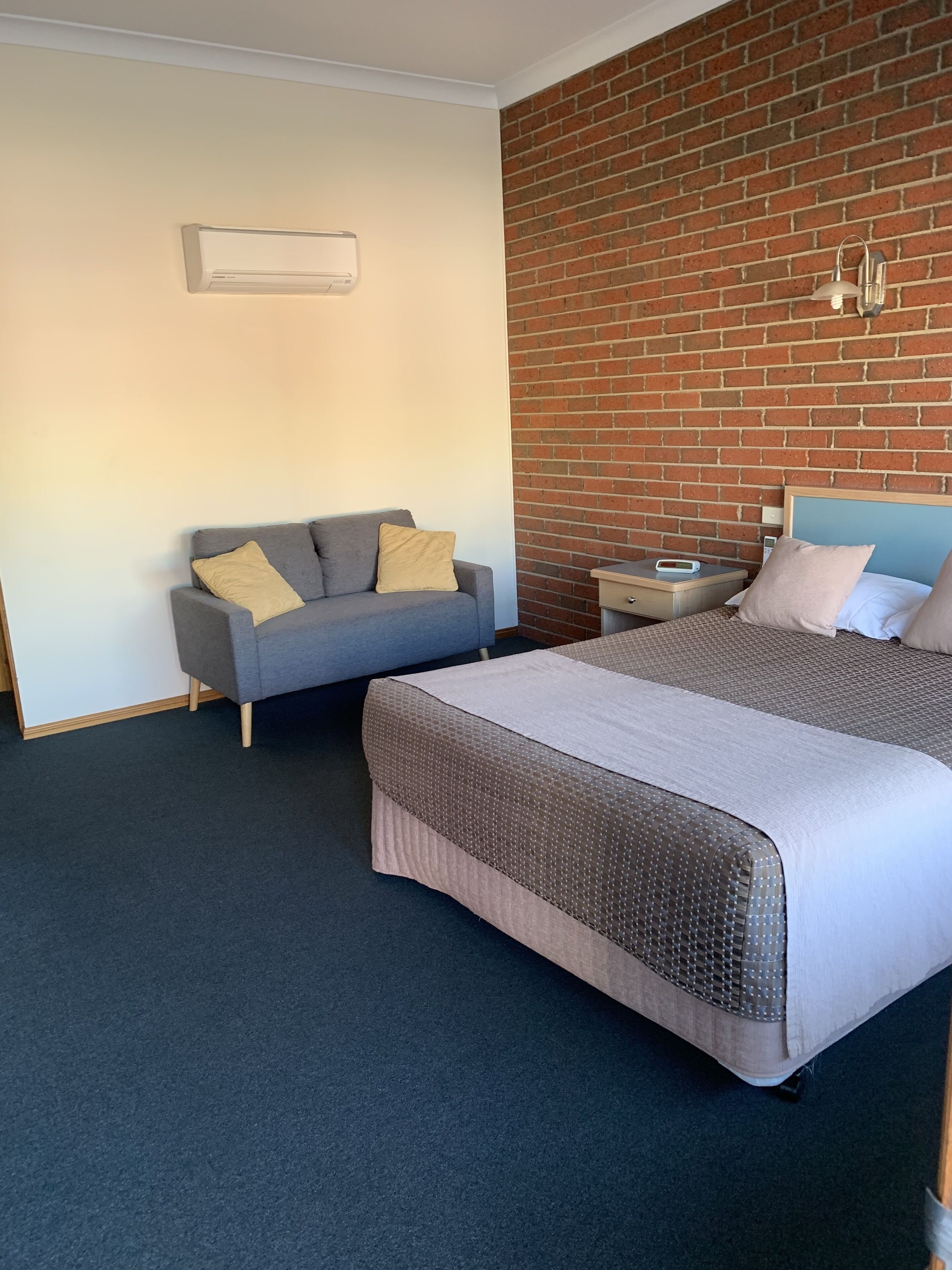 Une chambre d’hôtel avec un grand lit, un canapé gris, un mur en briques et une petite table avec une lampe.