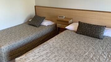 Two single beds with leaf-patterned bedding, a wooden headboard, and a bedside table with a digital clock.