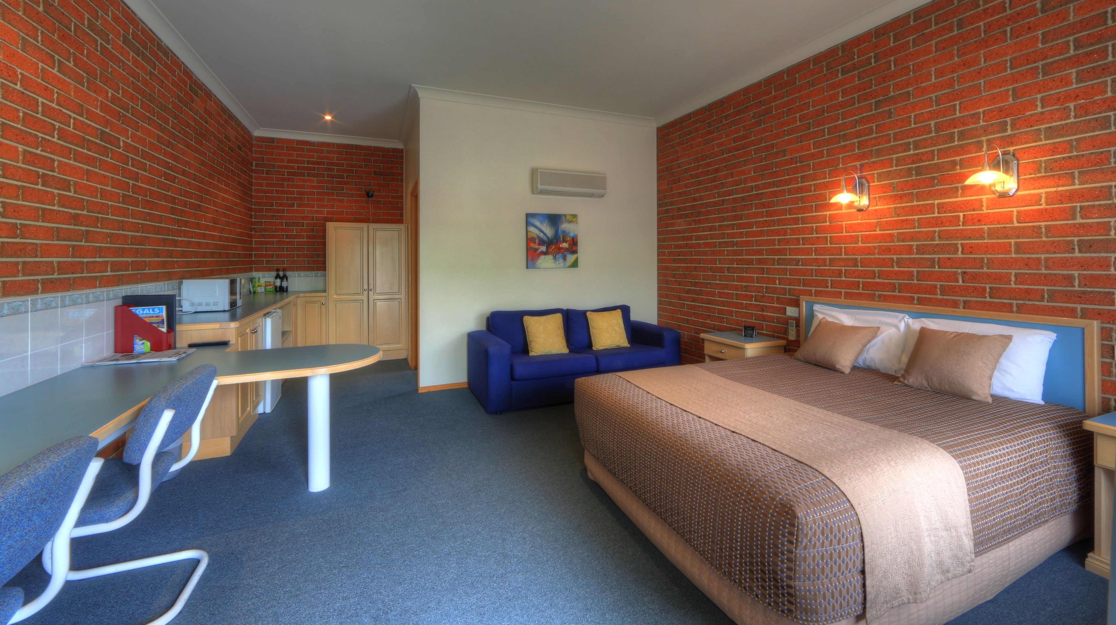 A hotel room with a bed, a blue sofa, a small desk, and a kitchenette.