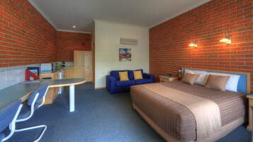 A hotel room with a bed, a blue sofa, a small desk, and a kitchenette.