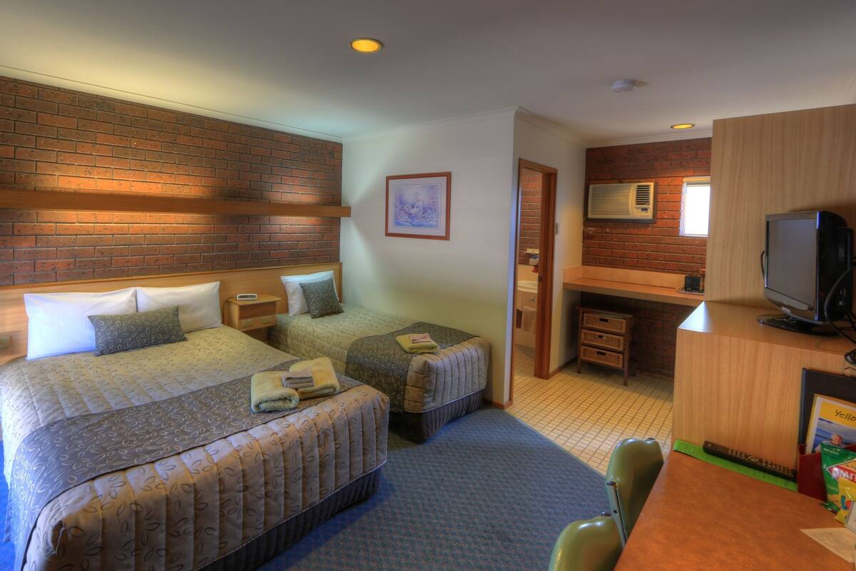 A hotel room with two beds, a small desk, a television, and a brick wall.