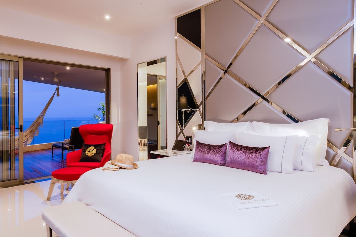 A spacious bedroom with a large bed, a red armchair, and a view of the ocean.