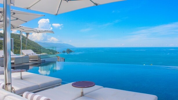 An infinity pool with white lounge chairs and umbrellas, overlooking a clear blue sea and distant mountains. - Hotel Mousai Puerto Vallarta Adults Only (Puerto Vallarta)