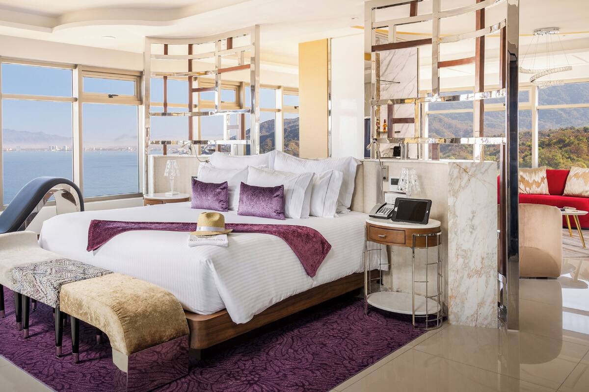 A modern bedroom with a large bed, a desk, and a view of the sea.
