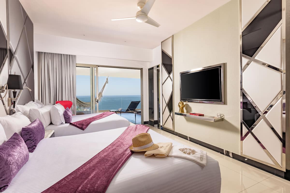 A hotel room with two beds, a TV, a ceiling fan, and a view of the ocean.